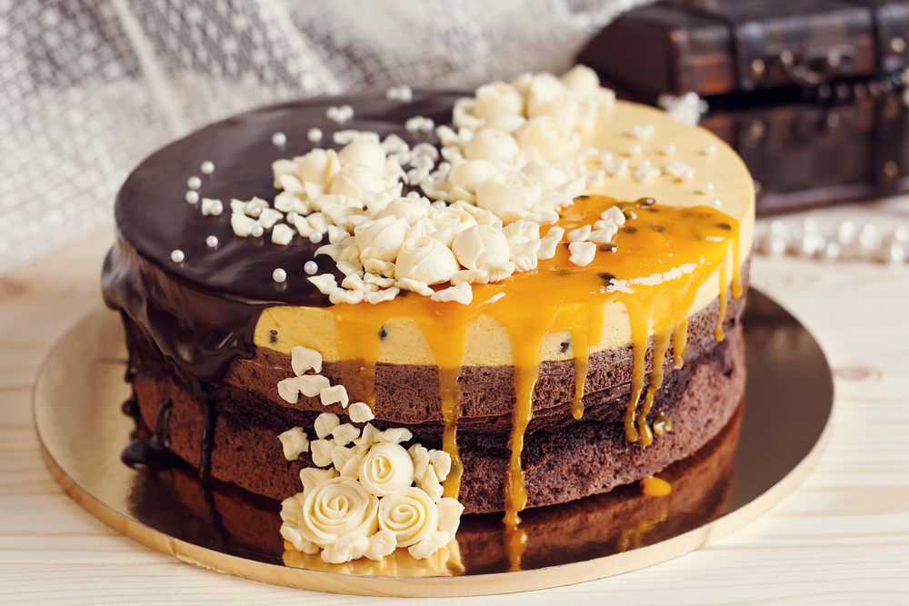 Romaantic cake with chocolate glaze, cream flowers and mango passionfruit mousse on retro background, vintage stylized photo